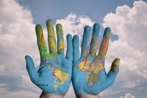 Zwei Hände mit aufgezeichneter Weltkarte im Hintergrund blauer Himmel und Sonnenschein
