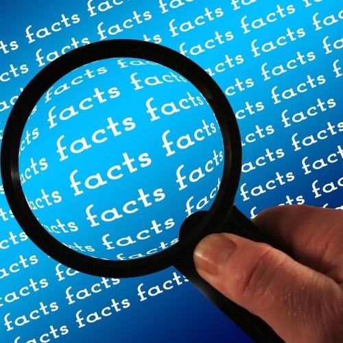 Hand mit Lupe, im Hintergrund mehrfach geschrieben der Begriff "facts"