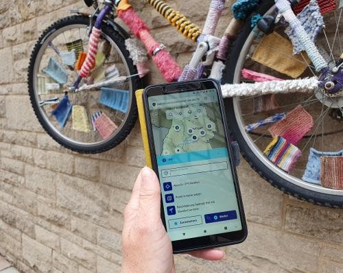 Hand mit Smartphone vor bestricktem Fahrrad
