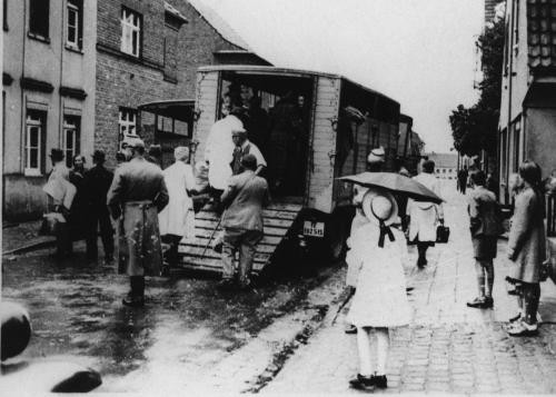 Schaulustige sehen zu, wie die Polizei Jüdinnen und Juden zur Deportation auf Lastwagen verlädt. Kerpen, Deutschland, 1942