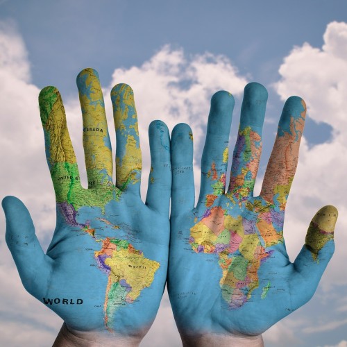 Zwei Hände mit aufgezeichneter Weltkarte im Hintergrund blauer Himmel und Sonnenschein